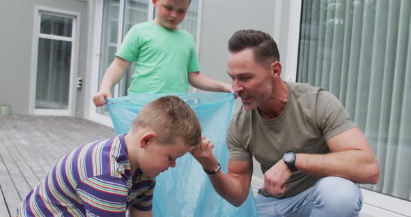 Caucasian father and two sons putting plastic materials in a bag outdoors