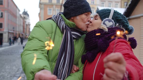 Senior Couple Holding Sparklers Bengal Lights Enjoying Christmas Eve Making Kiss in Winter City