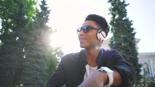 Portrait of Young Stylish Hipster Black Man in White Headphones and Sun Glasses Dancing Outdoor in