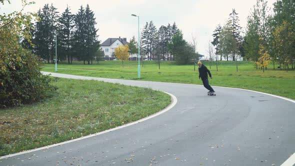 Adult Gray-haired Man Rides a Skateboard on a Path in a Forest Park, Autumn Time of the Year, Man