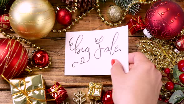 Woman's hand putting a Christmas card with the text BIG SALE on a wooden table