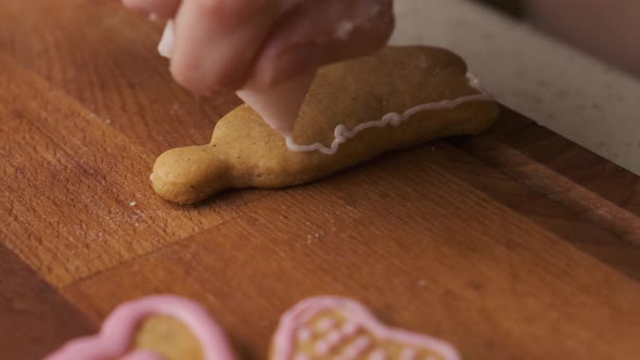 Woman Decorates a Gingerbread in the Shape of Bell on the Wooden Desk with Icing