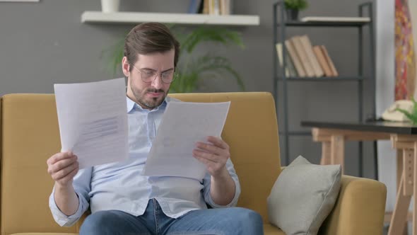 Young Man Reacting to Loss on Documents Sofa