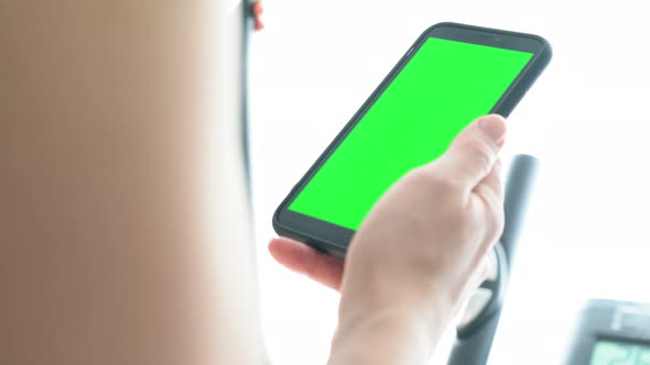 Young woman checking smartphone on cross trainer at home