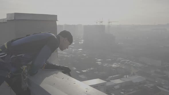 Man Climber in Special Form Stands on the Roof of a Tall House and Checks the Strength and Fastening