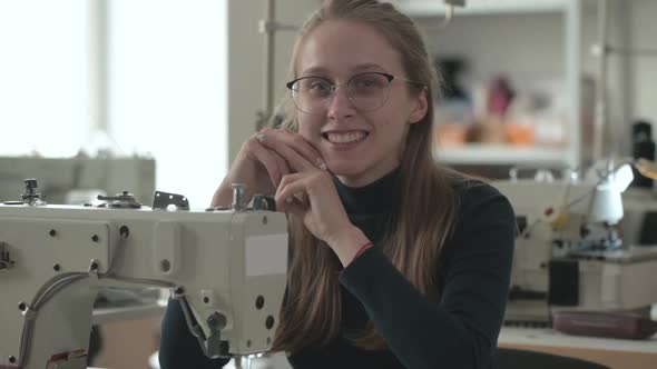 beautiful tailor sits at workplace with an electric sewing machine and smiles