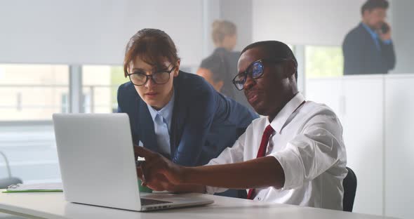 Diverse Man and Woman Working Together in Creative Office Using Laptop