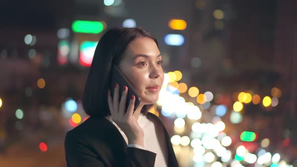 Asian young business woman standing outdoor using mobile phone downtown in city at night.