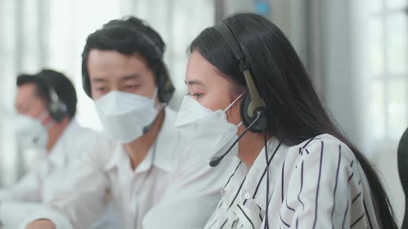 Man And A Woman Of Three Asian Call Centre Agents In Headsets And Masks Discussing About Work