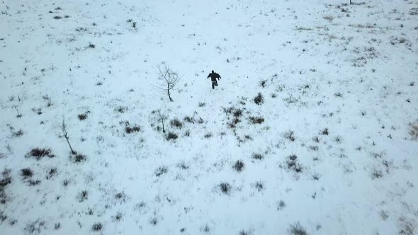 Man on the run in vast winter landscape, aerial follow shot, dark moody action scene