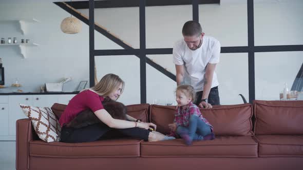 Portrait of Smiling Caucasian Man Admiring His Wife and Daughter Playing on Couch, Happy Blond Woman