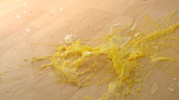 Dropping Glass of orange juice and breaking on wooden floor, Slow Motion alt