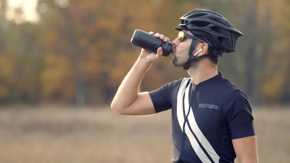 Cyclist In Helmet Relaxing After Workout Drinking Water. Fit Athlete Man Drinking Isotonic.