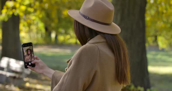 Back View of Young Caucasian Girl in Brown Hat and Coat Taking Selfie on Smart Phone