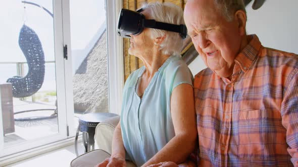 Front view of Caucasian senior woman using virtual reality headset and senior man siting on sofa at