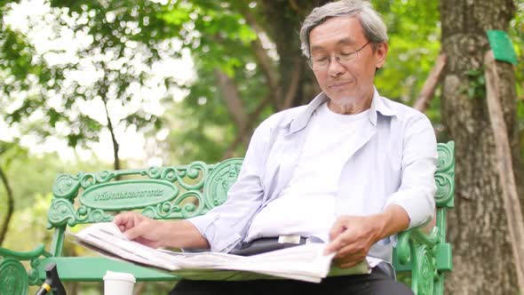 Asian senior man sitting in the park and reading a newspaper