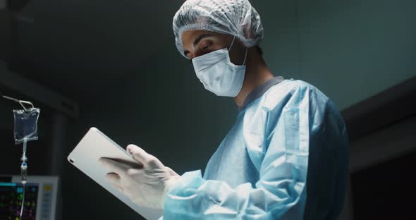 A Male Doctor in Sterile Clothing Uses a Digital Tablet in Intensive Careo