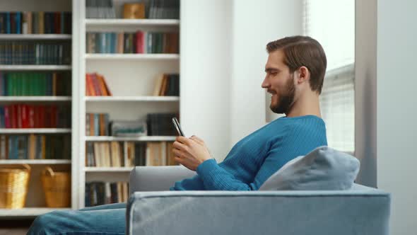 Young male typing on smartphone on sofa