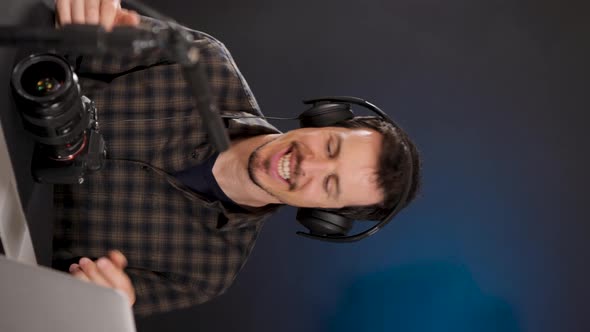 Cheerful guy inn headphones using laptop while recording vlog in studio