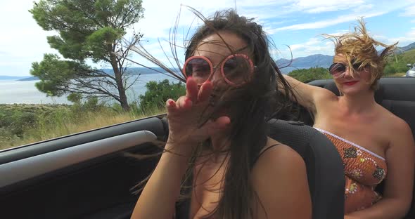 Two attractive women riding in cabriolet along dalmatian coast