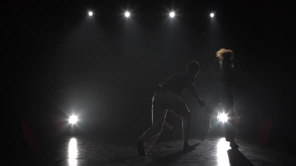 Woman and Man Practicing Capoeira in Darkness Against Spotlight in Studio