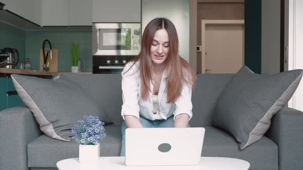 Excited Young Woman Winner Looks at Laptop Celebrates Online Success Sits on Sofa at Home