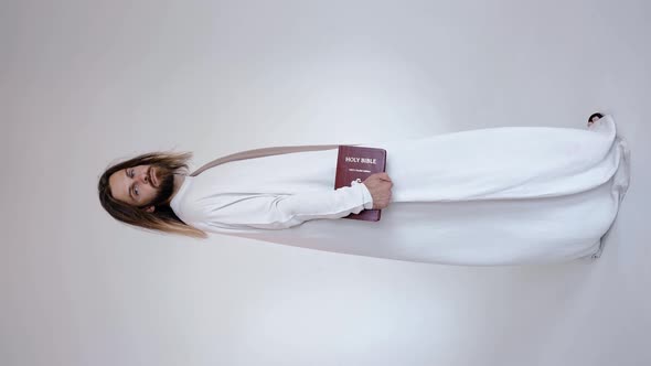 Jesus Looks Into the Camera Holding the Bible in His Hands on a White Background