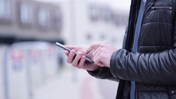 A Man Works on a Smartphone - Side Closeup - Suburban Area in the Blurry Background