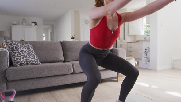 Woman performing squat exercise while using dumbbells at home