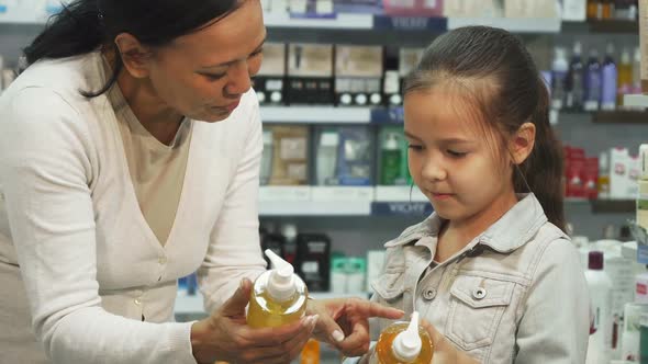 A Girl with Her Daughter Chooses Tubes of Cosmetic in a Pharmacy