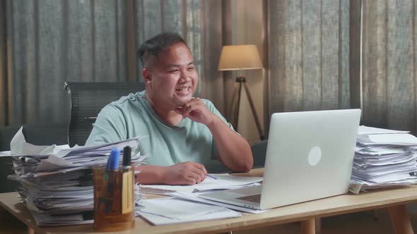 Fat Asian Man Having Video Call On Laptop While Working With Documents At The Office
