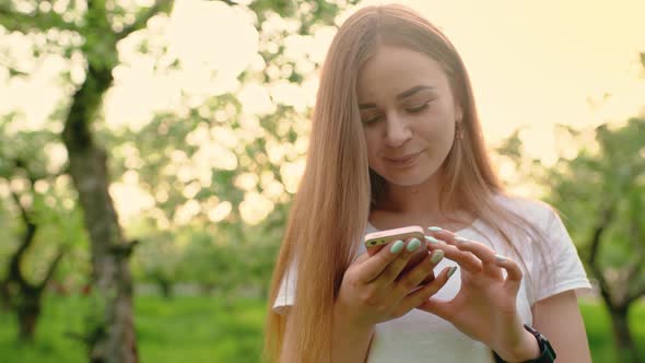 Portrait of a Beautiful Woman Typing on a Mobile Phone in the Park