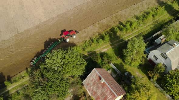 Farmer on a Tractor with a Plow Working Near the Village