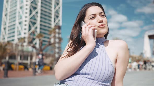 Smiling brunette woman talking by mobile while sitting on the bench