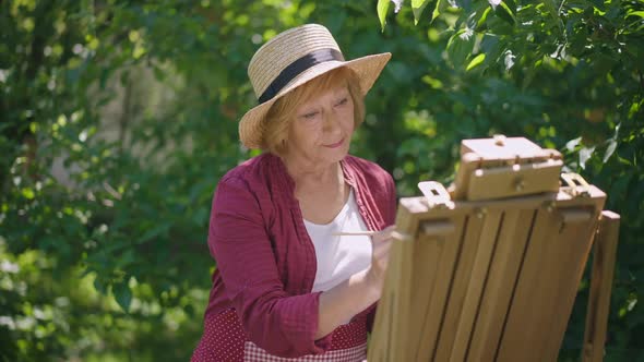 Thoughtful Senior Woman Painting in Sunshine Outdoors and Smiling Looking at Camera