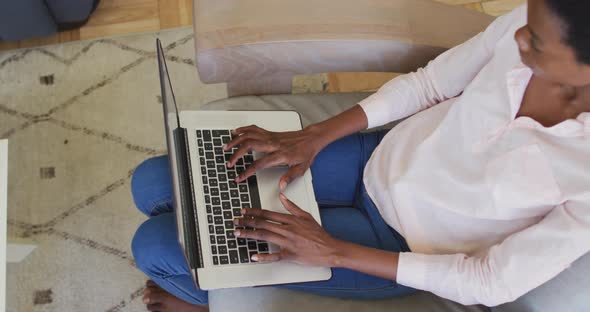 Happy african american woman sitting on armchair in living room, using laptop