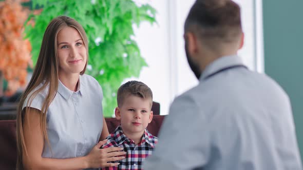 Portrait of Handsome Young European Mother and Little Son at Reception of Male Doctor