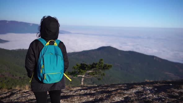 Young Redhead Woman Standing on a Rock High in the Mountains Above the Clouds and Enjoying the Warm