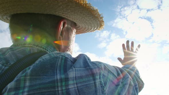 Farmer in Straw Hat Covering the Sun with Hand Standing on Sky Background