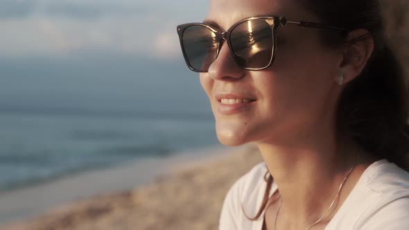 Portrait of Beautiful Smiling Woman in Sunglasses Looking at the Sea at Sunset.