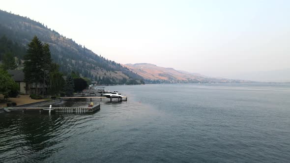 Aerial shot over Okanagan lake in Vernon, BC flying along the shore. Passing boats and small piers.