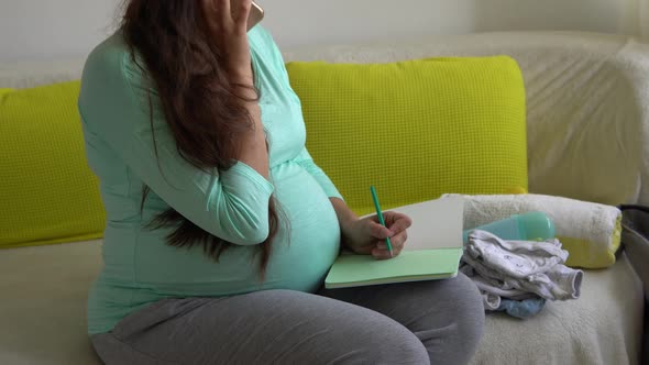 Cute Pregnant Woman Writing Packing List for Maternity Hospital With Notebook Prepares Bags