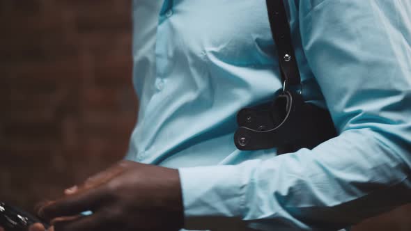 Close Up Portrait of African Cop Putting Gun in Holsters Isolated Over Brick Wall Background