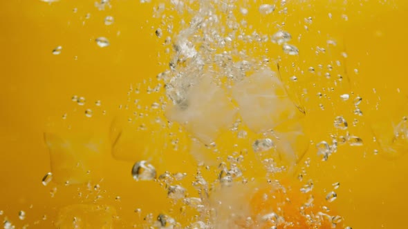 Closeup of Falling Ripe Oranges Into the Water with Ice on Orange Background Making a Cocktail of