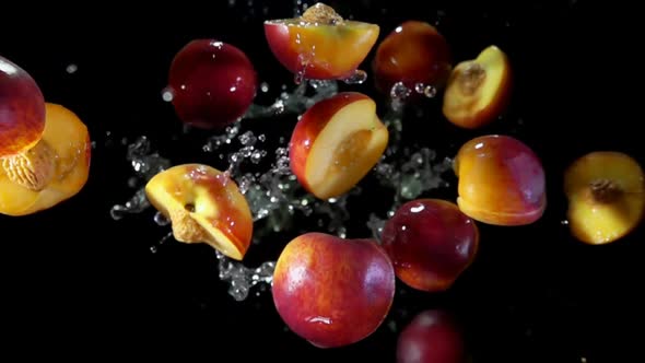 Halves of the Peach Are Bouncing with the Drops of Water on the Black Background