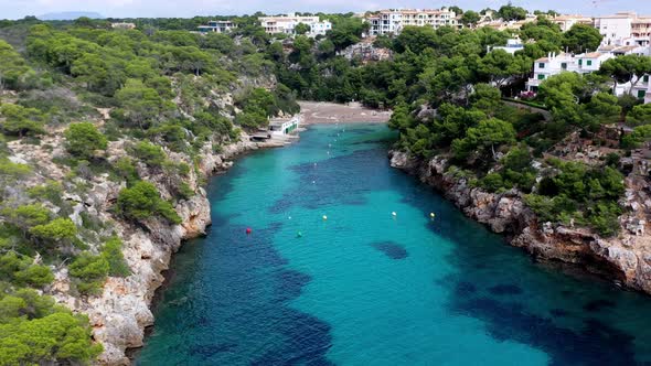 Cala Pi Beach in Mallorca Spain turquoise inlet with buoys and bathers, Aerial lowering approach sho