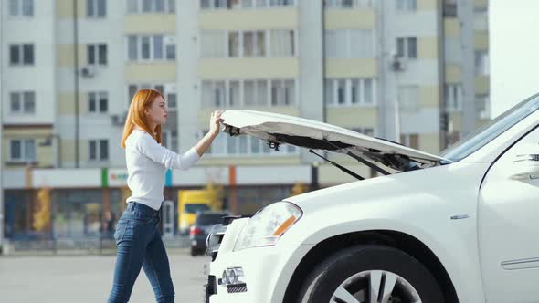 Young stressed woman driver near broken car with popped hood having a prbreakdown 