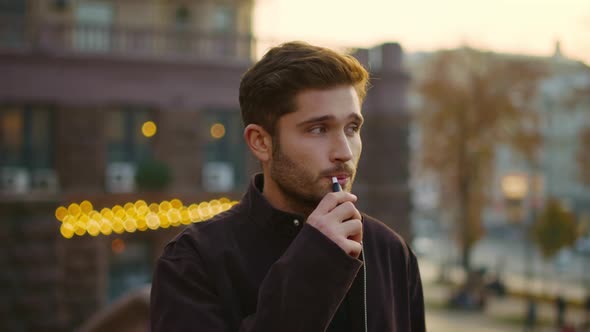 Serious Guy Smoking E-cigarette Outdoors. Thoughtful Man Vaping on Street.