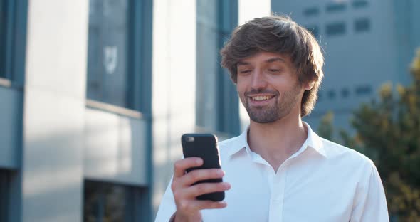 Handsome Caucasian Businessman is browsing his Smartphone, smiling Charmingly.