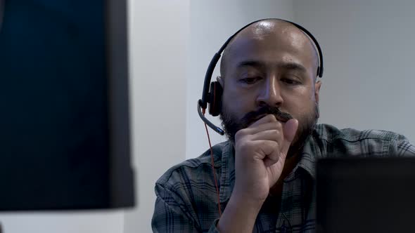 An Indian call centre employee seated at his office desk with his clutch fist covering his face, the